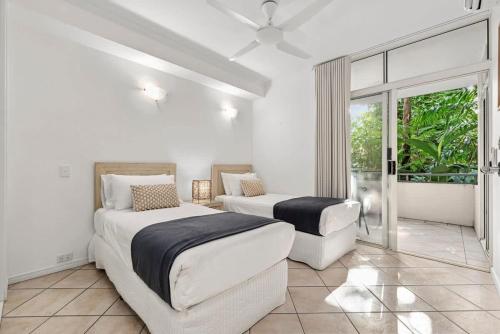 a white bedroom with two beds and a window at The MAGNA by Reef Stays in Palm Cove