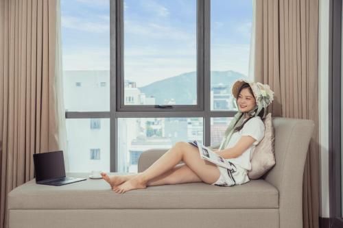 a woman sitting on a couch in front of a window with a laptop at Star Hotel and Spa Danang in Danang