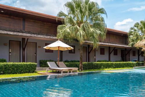 a pool with a chair and an umbrella next to a house at Malabar Pool Villa Phuket in Phuket Town