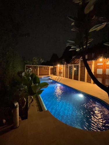 a swimming pool at night with a palm tree at Bale Devata Resort in Sleman
