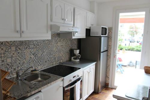 une cuisine avec des armoires blanches, un évier et un réfrigérateur dans l'établissement Appartement T3, avec terrasse, place de parking privée, à Saintes-Maries-de-la-Mer