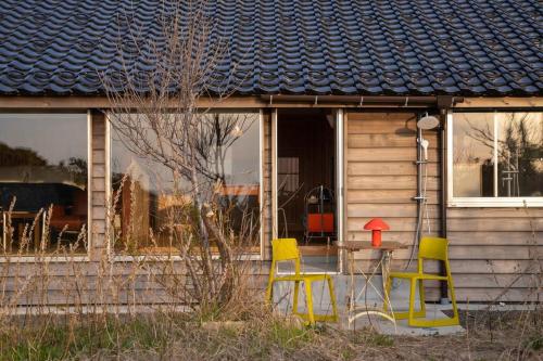 two yellow chairs and a table in front of a house at Captain's House, explore the crustal movement every thousand years in Kuroshima