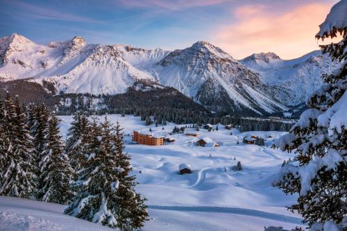 a snowy mountain range with a lodge in the foreground at Golf- & Sporthotel Hof Maran in Arosa