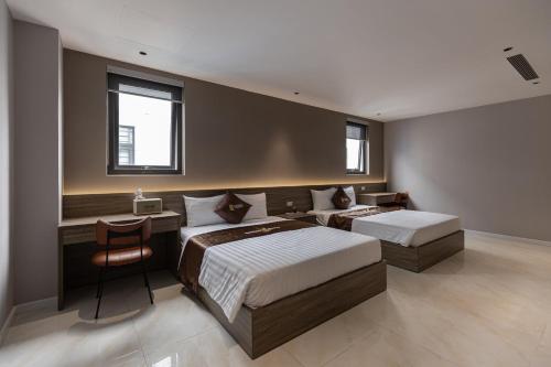 a bedroom with two beds and a desk and two windows at Luxhome Mekong Hotel in Can Tho