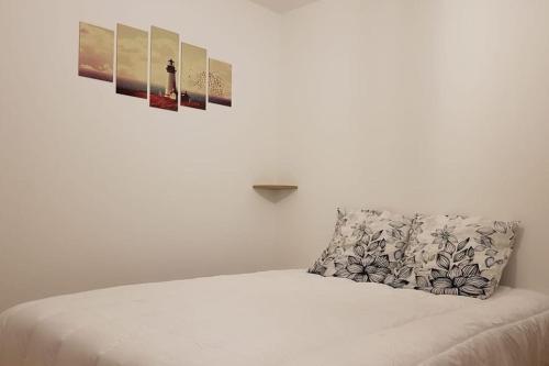 a white bed with a pillow and pictures on the wall at Erquy, vue mer, centre, plages & commerces a pieds in Erquy