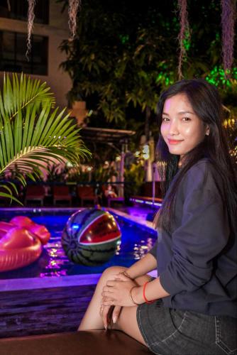 a woman sitting on a table in front of a pool at Bliss & Beats Hostel in Phnom Penh