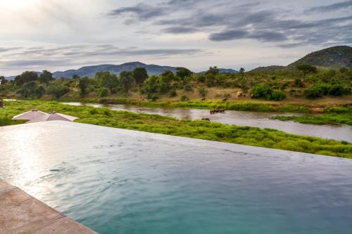 a swimming pool with a river and mountains in the background at Royal Mukumbura Malelane in Malelane