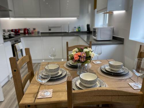 a wooden table with plates and glasses and flowers on it at Hatfield Haven - Modern 2-Bed Retreat near Uni, Business Park & City Center, FREE Parking, Big savings on Longer Stays in Hatfield