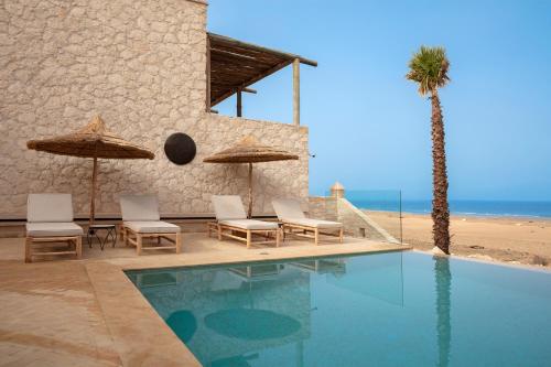 a pool with chairs and umbrellas next to the beach at Kasbah d'Eau in Sidi Kaouki