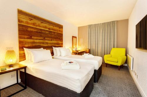 a hotel room with two beds and a yellow chair at Cedar Court Bradford Hotel in Bradford