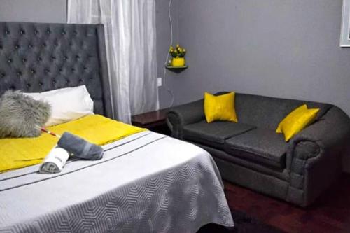 a bedroom with a bed with yellow pillows and a couch at The Adventure Begins in Bulawayo