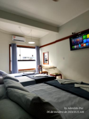 a room with three beds and a television on the wall at Hotel São Charbel in Ubatuba