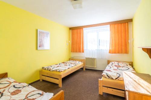 two beds in a room with yellow walls and a window at Penzion Vápenka in Horní Maršov