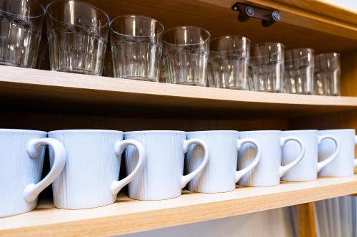 a row of coffee mugs on a shelf with glasses at The CATAN 石垣島 in Nagura