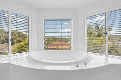 a white bathroom with a large tub in front of windows at Exclusive Luxury Oasis Tumbi Umbi NSW in Berkeley Vale
