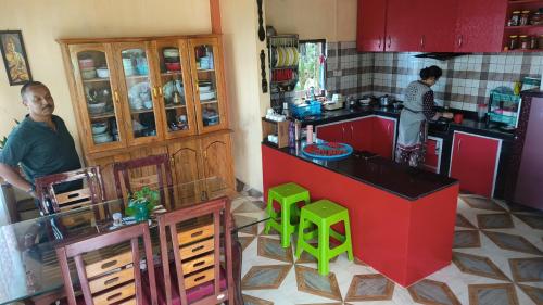 two people in a kitchen with red cabinets and green stools at Goo Sheela Homestay in Darjeeling