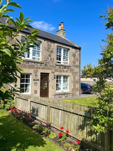 an old stone house with a fence and flowers at The Furze Farmhouse near St Andrews in Newburgh