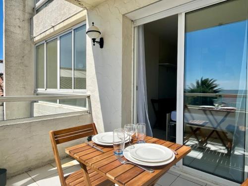 une table en bois avec des assiettes et des verres sur un balcon dans l'établissement Studio vue mer Saint Palais sur Mer, à Saint-Palais-sur-Mer