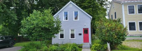 a gray house with a red door in a yard at Sparrowhawk House in Yarmouth