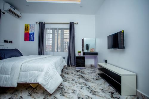 a white bedroom with a bed and a television at Aija Residences in Abuja