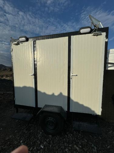 a white trailer with its door open on a gravel road at The Out in Sinādil