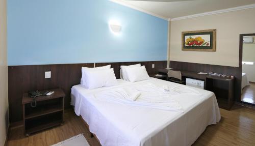 een slaapkamer met een groot wit bed en een blauwe muur bij Hotel Jaguar in Uberaba