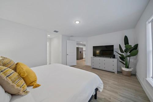 a white bedroom with a large bed and a television at New Construction Home 10 to Beach 5 to Downtown in West Palm Beach