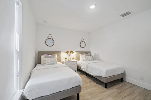 two beds in a bedroom with white walls and wood floors at New! Few Minutes To Downtown, 10 To The Beach! in West Palm Beach