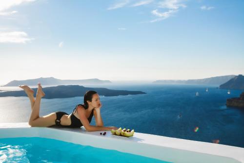 a woman laying on the edge of a swimming pool at Alti Santorini Suites - Caldera View in Megalochori