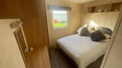 a small bedroom with a bed and a window at PG69 Golden Palm 8 Berth Caravan with Decking in Chapel Saint Leonards
