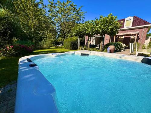 a large blue swimming pool in front of a house at Luxe vakantievilla met jacuzzi in Zeewolde