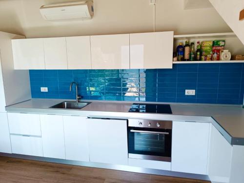 cocina con armarios blancos, fregadero y azulejos azules en Grandin Holidayhouse, en Domaso