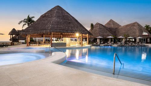 a pool at a resort with thatched umbrellas and chairs at Hard Rock Hotel Riviera Maya - All Inclusive in Puerto Aventuras