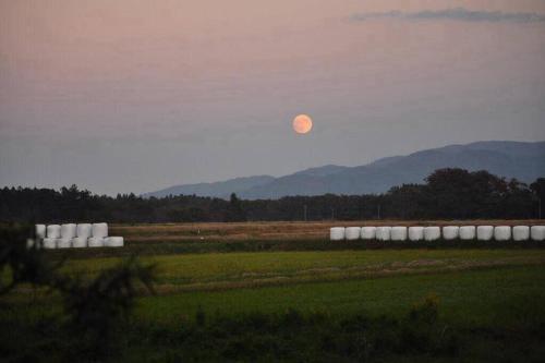 a moon in the sky over a field with a farm at 一棟貸切 古民家民泊あさひ in Sado