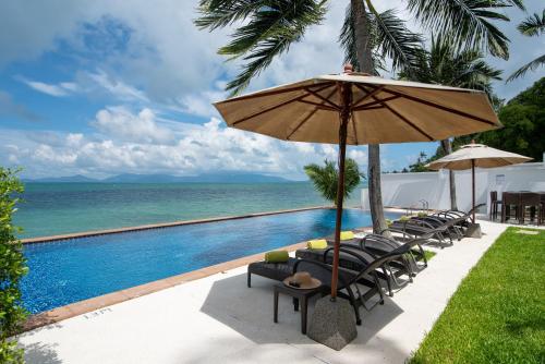a pool with chairs and an umbrella and the ocean at Lotus Samui Luxury Beach Villas in Mae Nam
