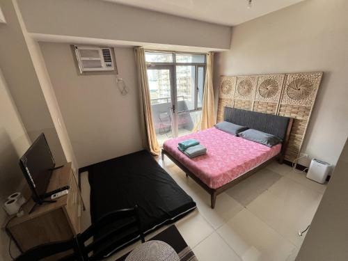a small bedroom with a pink bed and a window at Cubao Manhattan Heights Residential Condo TC10N - Bright Studio with Pool, Balcony - Next to AliMall and SM - Walking Distance to Araneta Coliseum and Gateway Mall in Cubao Quezon City - Staycations by SMS in Manila