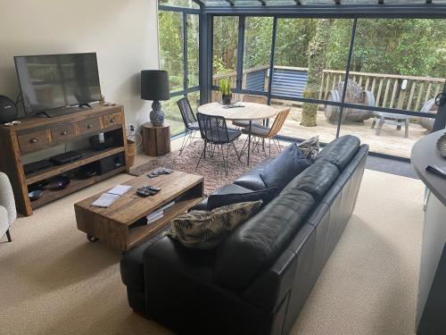 a living room with a black leather couch and a table at Love Punakaiki Luxury Couples Retreat Limited in Punakaiki