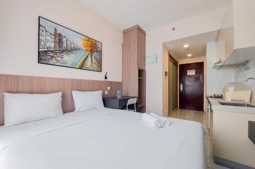 a bedroom with a large white bed and a kitchen at Comfy and Best Choice Studio at Sky House BSD Apartment By Travelio in Tangerang