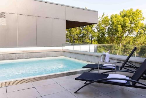 a swimming pool with two chairs and a table at Live Hotels Bordeaux Lac in Bordeaux