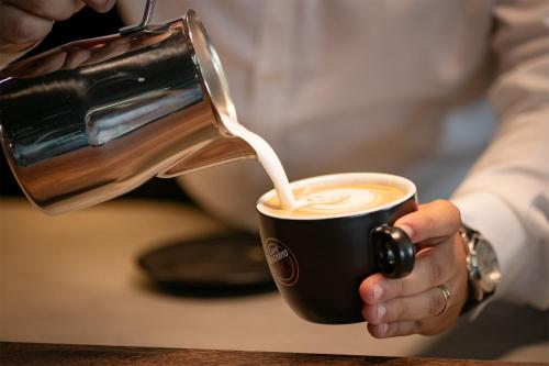 a person pouring milk into a cup of coffee at Electra Aparthotel in Rădăuţi