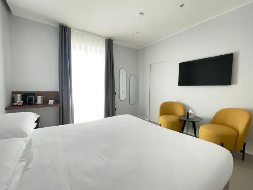 a bedroom with a white bed and two yellow chairs at OMÍ Aparthotel in Caserta