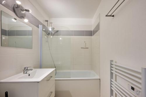 une salle de bain blanche avec un lavabo et une baignoire dans l'établissement Les Jardins du Val Pican - Appt proche de la mer, à Courseulles-sur-Mer