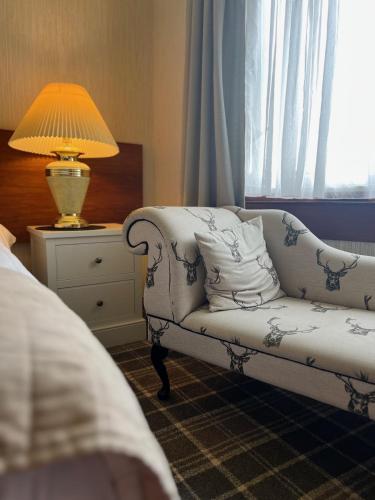 a bedroom with a couch and a lamp on a night stand at Loch Ness Lodge Hotel in Drumnadrochit