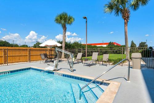 a swimming pool with chairs and an umbrella and palm trees at Hampton Inn & Suites Pensacola I-10 N at University Town Plaza in Pensacola