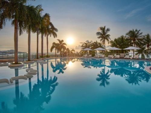 a swimming pool with palm trees and the sunset at Mövenpick Hotel Mactan Island Cebu in Mactan
