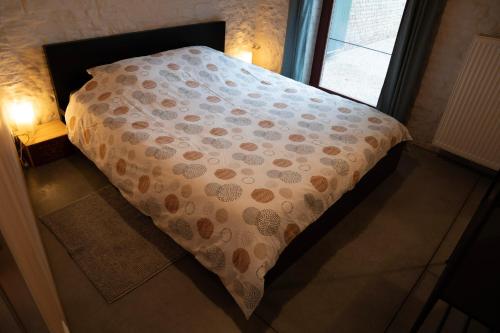 a bed with a comforter on it next to a window at La Dame Jeanne in Brakel