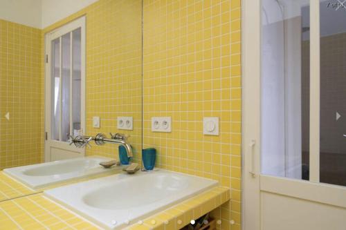 - une salle de bains carrelée de jaune avec lavabo et miroir dans l'établissement Charmant Appartement à Montmartre, à Paris