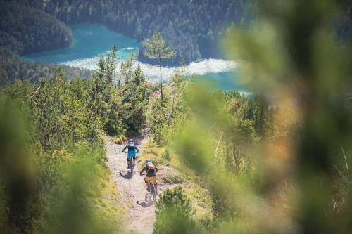 two people riding bikes on a dirt trail with a lake at Alpenchalets Biberwier Zugspitze by ALPS RESORTS in Biberwier