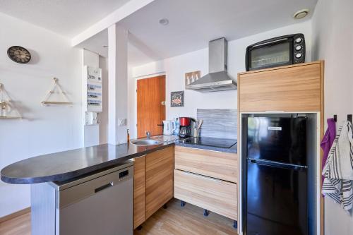 a kitchen with a black refrigerator and wooden cabinets at Le Côtier - Appt à 200m de la plage in Courseulles-sur-Mer