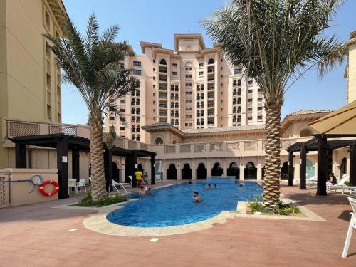 a large building with palm trees and people in a swimming pool at Free housekeeping visits during your stay - StayShort - Restful 1-Bedroom Apartment at Al Andalus in Jumeirah Golf Estates in Dubai